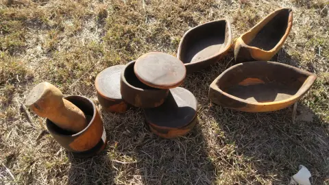 Carved wooden bowls, lidded pots and a mortar and pestle on the grass