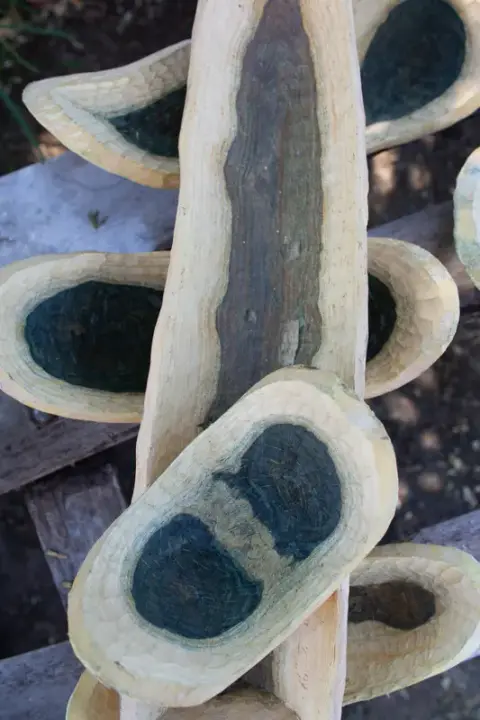Rough-carved wooden bowls with dark green-black centres, stacked on a board