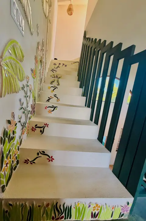 White stairs climbing past a mosaic wall of palms and flowers, with a mosaic sprig on every step