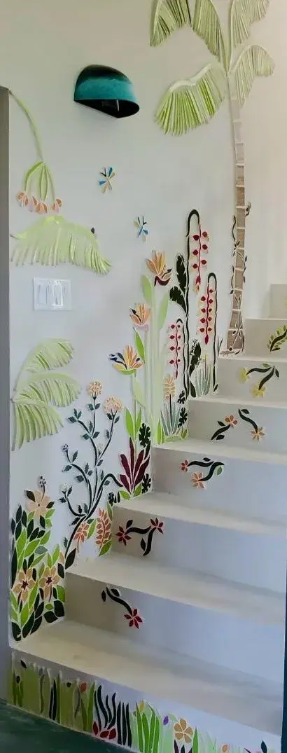 A staircase wall covered in a mosaic garden of palms, flowers and a dragonfly, with mosaic vines on the steps