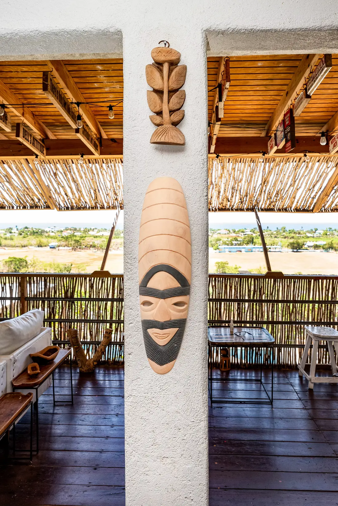 Two carved wooden masks on a white pillar, with the countryside and sea seen from the balcony behind them