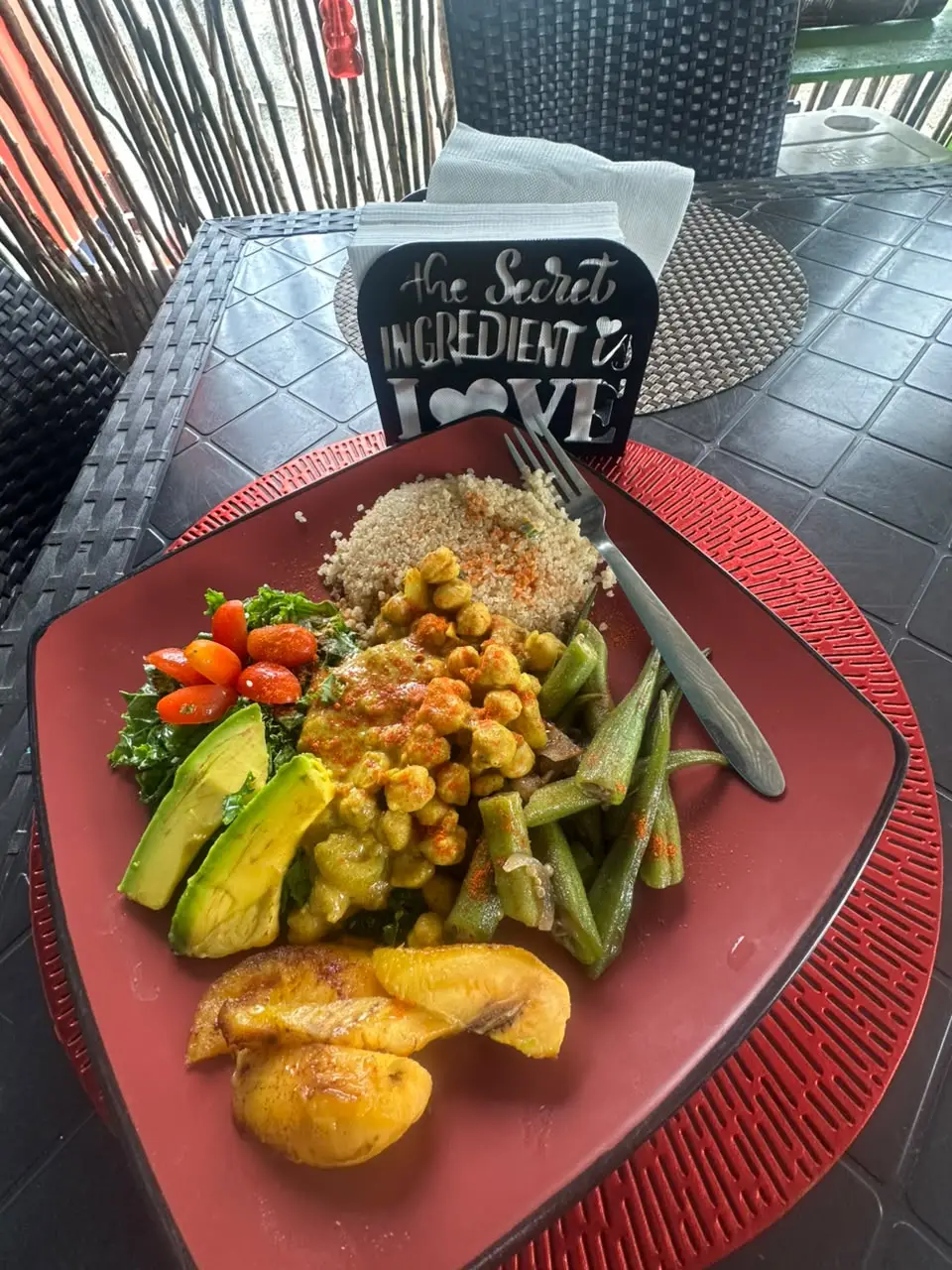 A plate of curried chickpeas, quinoa, okra, kale salad with cherry tomatoes, sliced avocado and fried plantain